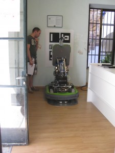 FROG robot on its stainless steel docking station, surrounded by wood laminate floor