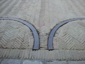 transition from patterned cobblestones in concrete over row of stone flags onto herringbone pattern laid brick with deep-set gate wheel tracks with wooden fillers