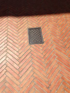 drain cover set in smooth red bricks herringbone laid